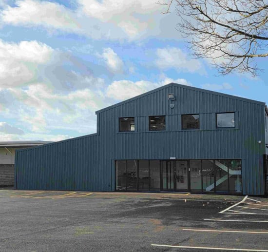 UK home exterior building with modern blue cladding and large windows, under a partly cloudy sky.